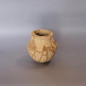 May include: A small, brown, earthenware pot with a rounded body and a slightly flared rim. The pot has a crackled glaze and is decorated with brown streaks.