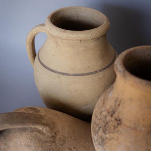 May include: Three terracotta clay pots with a rustic, aged appearance. The pots are various sizes and shapes, with one featuring a brown stripe around the middle.