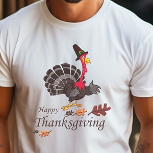 Może przedstawiać: Biała koszulka z kreskówkowym indykiem w kapeluszu pielgrzyma i napisem "Happy Thanksgiving".