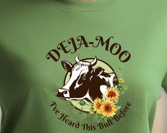 May include: Green t-shirt with a brown and white cow graphic and the text "Deja-Moo I've Heard This Bull Before".