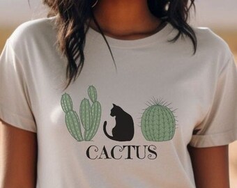 May include: A light grey t-shirt with a graphic of three cacti and a black cat sitting on one of the cacti. The text "Cactus" is printed below the graphic.