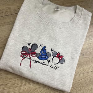 Peut inclure: Sweat-shirt gris clair avec broderie d'oreilles de souris de dessin animé, d'un chapeau de magicien et d'un nœud. Le texte brodé "Some imagination, huh?" est en dessous. Le sweat-shirt est en matière douce.