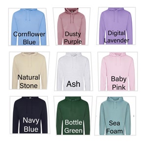May include: Nine different coloured hooded sweatshirts are displayed, including Cornflower Blue, Dusty Purple, Digital Lavender, Natural Stone, Ash, Baby Pink, Navy Blue, Bottle Green, and Sea Foam. Each has a drawstring hood.
