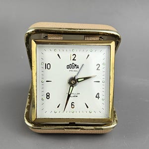 Dogma reseväckarklocka med mekanisk clamshell-design. Samlarobjekt i vintage-stil.