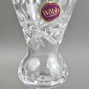 May include: Clear lead crystal vase with a flared top and a bulbous midsection, resting on a circular base. The vase features intricate diamond and starburst cut patterns. A purple and gold label reads "Webb continental Hand Cut Lead Crystal Czechoslovakia."