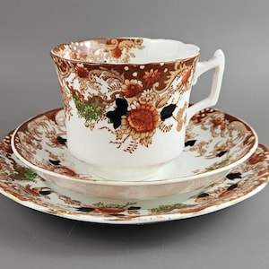 Puede incluir: Un juego de té vintage que incluye una taza, un platillo y un plato. Las piezas de porcelana blanca presentan un diseño floral marrón con detalles en naranja y negro. Para servir té.