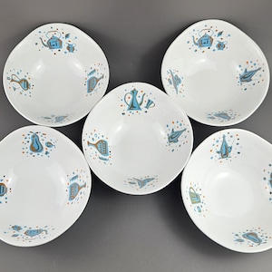 Puede incluir: Cinco cuencos de cerámica blanca con una forma asimétrica inusual. Cada cuenco presenta un patrón repetido de ilustraciones azules, naranjas y marrones de teteras, peras y otros objetos de cocina. Los cuencos están dispuestos sobre una superficie gris.