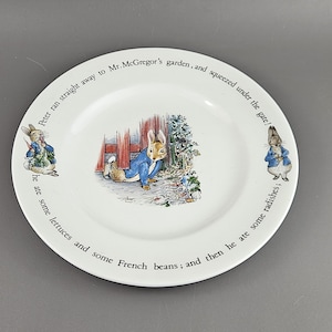 May include: White ceramic plate with illustrations of Peter Rabbit in a blue jacket, and text around the rim. The plate depicts scenes from a children's story, with text that reads "Peter ran straight away to Mr. McGregor's garden, and squeezed under the gate!"