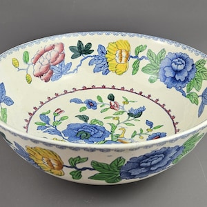 Puede incluir: Cuenco de cerámica color crema con diseño floral. El cuenco presenta flores y hojas azules, amarillas, rosas y verdes. El borde tiene un delicado patrón azul y blanco. Una pieza decorativa para servir o exhibir.