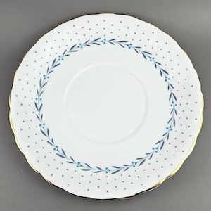 Könnte beinhalten: Weiße Untertasse mit einem gewellten Goldrand. Sie hat ein zartes blaues Blumenkranz-Design und kleine blaue Kreuzmuster. Ein klassisches Stück zum Servieren, mit einem Durchmesser von etwa 15 cm.