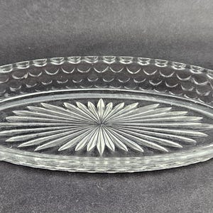 Puede incluir: Fuente ovalada de vidrio transparente con asas. La fuente presenta un diseño de estrella en el centro y un borde festoneado. Las asas son curvas. Una pieza decorativa para servir.
