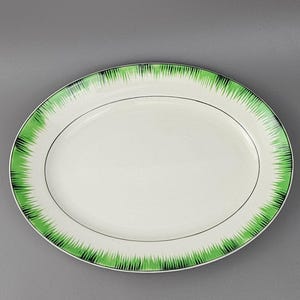 May include: Oval serving platter with a white centre and a decorative border featuring a green and black grass-like pattern. A thin black line encircles the centre. The platter is on a grey background.