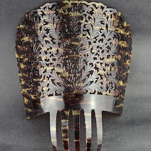 Könnte beinhalten: Ein dekorativer Haarkamm mit detailliertem floralem Design. Der Kamm hat ein dunkelbraunes, schildpattartiges Muster mit Akzenten in Gold und Silber. Der obere Teil hat ein offenes Design und der Kamm hat mehrere Zähne.