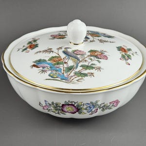 May include: White ceramic serving dish with lid, featuring a colorful floral and bird design. The lid has a white knob and gold trim. The dish has a scalloped edge and is decorated with flowers and a peacock.