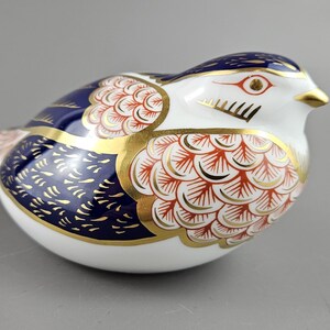 Puede incluir: Figurita de pájaro de cerámica con base blanca, adornada con intrincados diseños en azul marino, rojo y dorado. Las alas del pájaro presentan un diseño detallado de plumas y el pico es dorado. Artículo decorativo.
