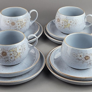 May include: Four matching sets of light blue teacups and saucers. Each cup and saucer has a speckled finish and a floral design in white and brown. The rims of the saucers and cups are trimmed in gold.