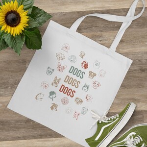 Könnte beinhalten: Weiße Stofftasche mit einem Kreis aus Hundefiguren in verschiedenen Farben und Rassen. Der Text "DOGS DOGS DOGS" ist in der Mitte des Kreises gedruckt.