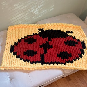 May include: A yellow, red, and black knitted blanket with a ladybug design.