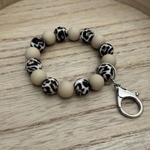 Può includere: Un portachiavi con perline beige e marroni con stampa leopardata e un moschettone argentato.