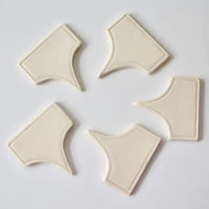 May include: Five off-white ceramic tiles with a decorative border and a pointed tip. The tiles are arranged in a circle.