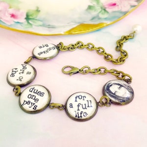 以下が含まれることがあります： 丸いチャームとチェーンが付いたヴィンテージスタイルのブレスレット。チャームにはテキストと白黒の肖像画が描かれています。ブレスレットはブロンズ仕上げで、チェーンの端にはパールのアクセントが付いています。