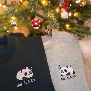 Könnte beinhalten: Zwei schwarze und graue Sweatshirts mit gestickten Pandabären. Der schwarze Pullover hat eine rosa Schleife auf dem Panda und den Text "Ms. Lazy". Der graue Pullover hat den Text "Mr. Lazy".