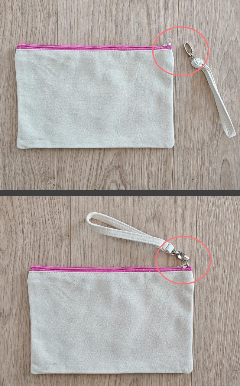 May include: A white canvas zippered pouch with a pink zipper and a white strap with a silver clasp. The pouch is lying flat on a wooden surface.