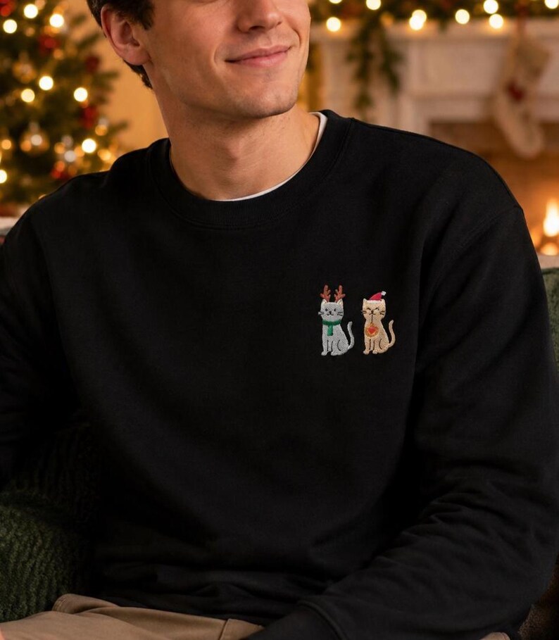 Mann trägt einen Katzen Weihnachts Hoodie mit kleiner Stickerei vor weihnachtlichem Hintergrund.
