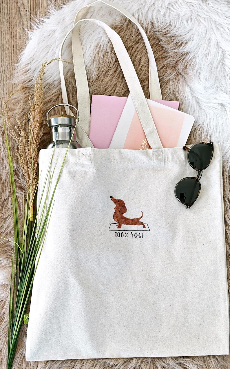 Puede incluir: Una bolsa de lona blanca con un dachshund marr&oacute;n haciendo yoga en una estera y el texto "100% YOGI".
