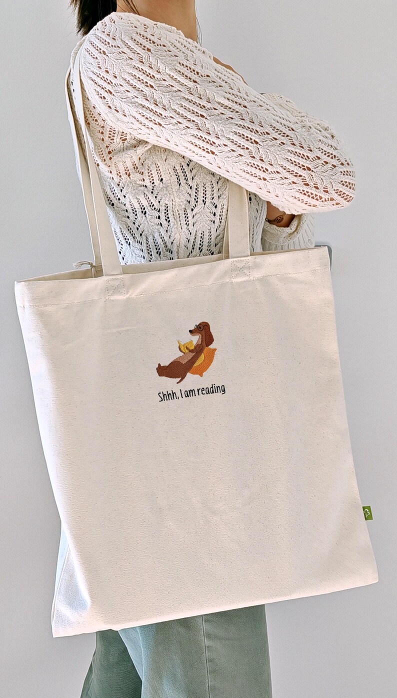Puede incluir: Una bolsa de lona blanca con un perro salchicha marr&oacute;n leyendo un libro y el texto "Shhh... I am reading".