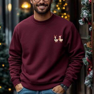 Mann trägt lustigen Weihnachtspullover mit bestickter Ente oder Gans in gemütlicher Weihnachtsatmosphäre.