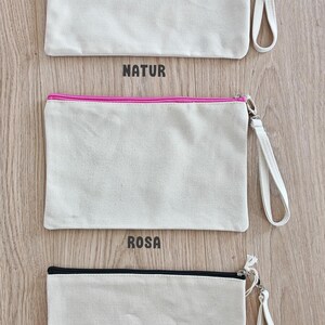 May include: Three canvas zipper pouches with a zipper pull and a strap. The pouches are all the same size and shape. The top pouch has the word "NATUR" printed below it. The middle pouch has the word "ROSA" printed below it. The bottom pouch has the word "SCHWARZ" printed below it.