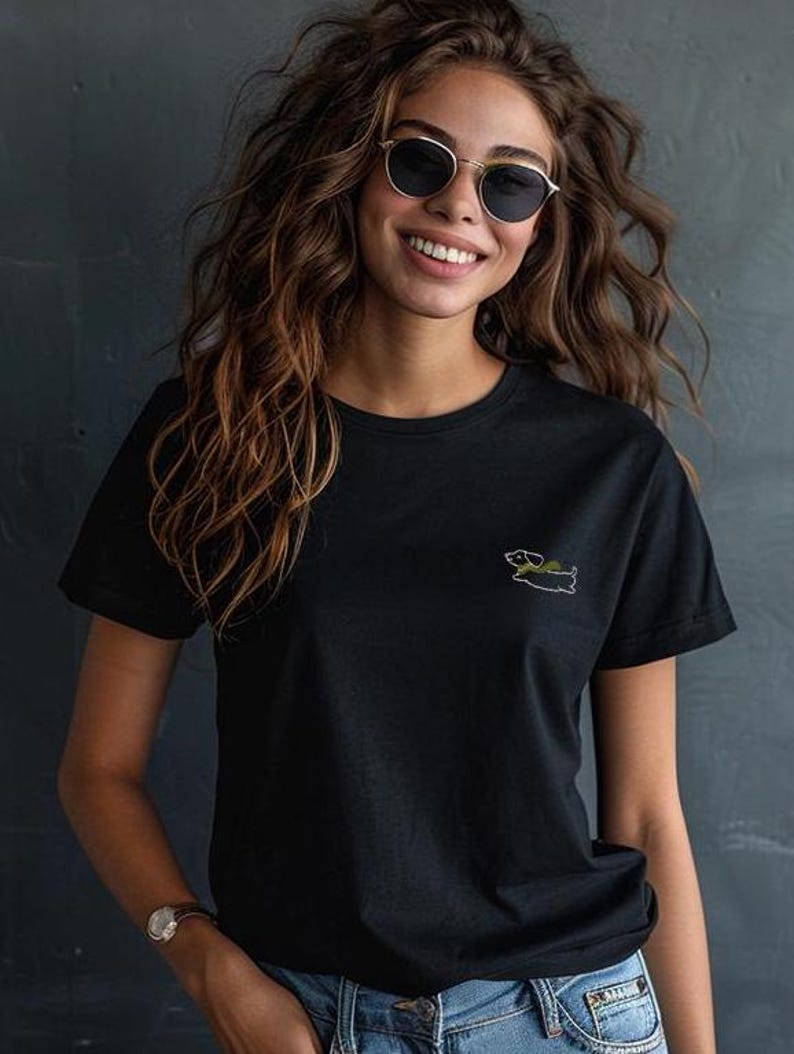 May include: A black t-shirt with a small embroidered image of a dachshund wearing a green hat.