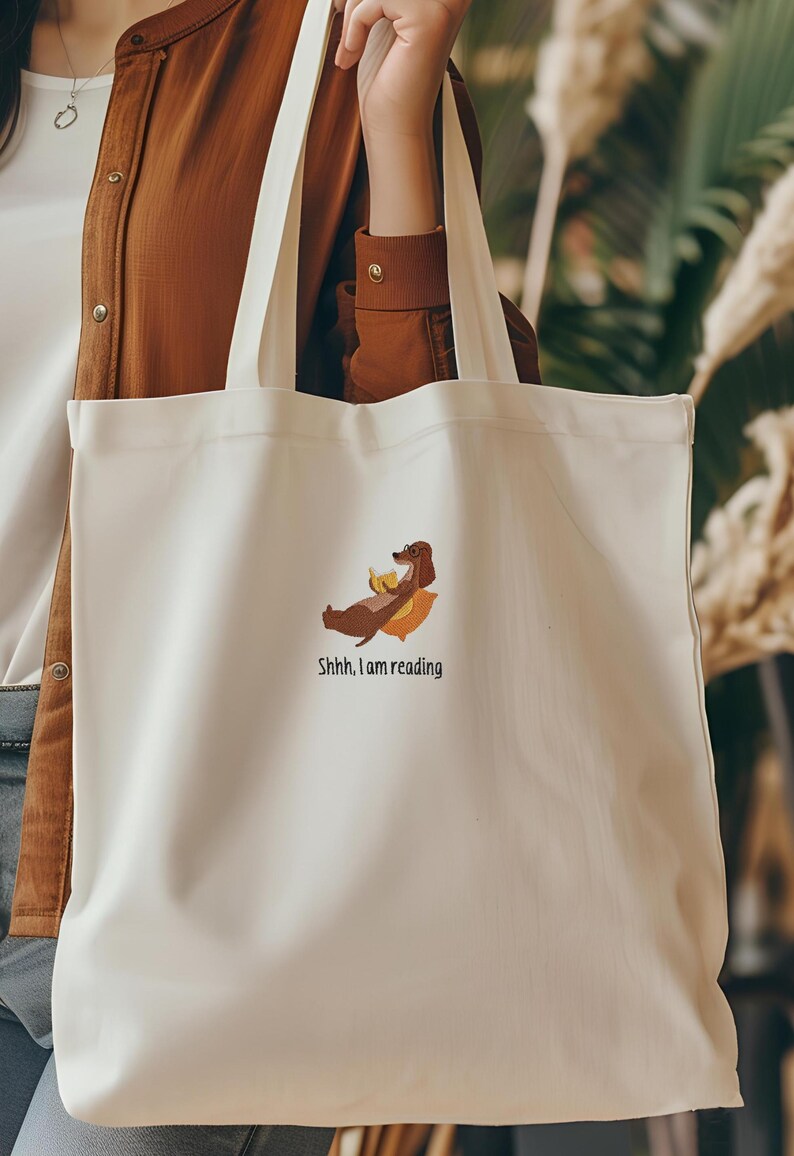 Puede incluir: Una bolsa de tela blanca con una ilustraci&oacute;n de un perro salchicha marr&oacute;n y el texto "Shhh, estoy leyendo".
