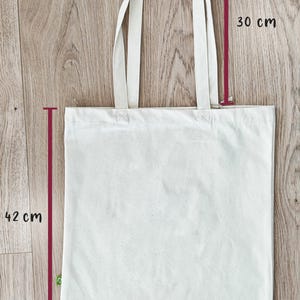 Puede incluir: Una bolsa de tela de lona blanca con dos asas. La bolsa mide 38,5 cm de ancho, 30 cm de alto y 42 cm de largo.