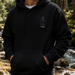 Op de afbeelding: Een zwarte hoodie met een witte lijntekening van twee beren die elkaar omhelzen met een klein roze hartje erboven en het woord always in cursief schrift onder de beren op de linkerzijde van de borst.