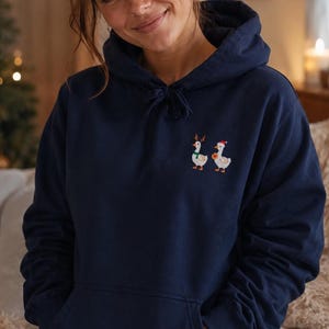 Frau trägt bestickten Weihnachts Hoodie mit süßer Ente vor weihnachtlichem Hintergrund, Geschenkidee für Tierliebhaber.