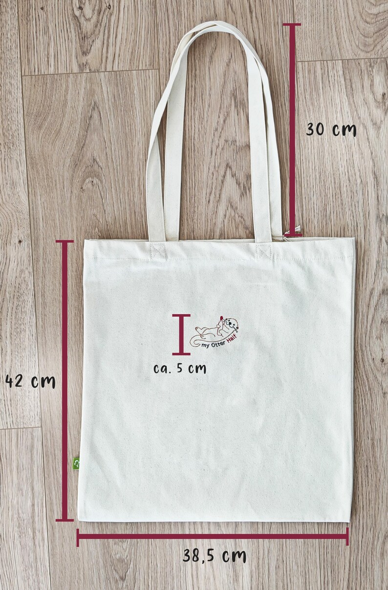 Puede incluir: Una bolsa de tela blanca con un gr&aacute;fico de una nutria y el texto "I my Otter Half". La bolsa mide 42 cm de alto, 38,5 cm de ancho y tiene asas de 30 cm. El gr&aacute;fico mide aproximadamente 5 cm.