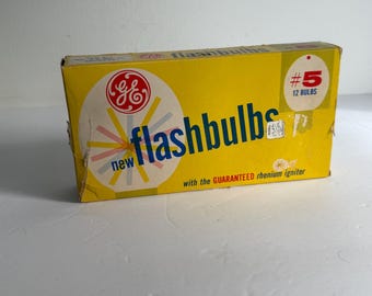 May include: A vintage yellow box of GE flashbulbs. The box features the GE logo and the words "flashbulbs" in blue. The box also indicates it contains 12 bulbs, size #5, and has the text "with the GUARANTEED rhenium igniter."