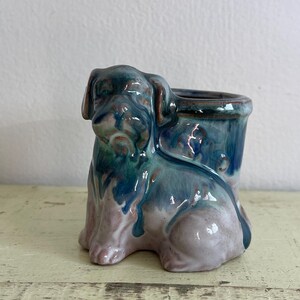 May include: A small ceramic planter shaped like a dog. The planter is glazed in shades of blue, green, and pink.