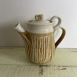 May include: A white ceramic teapot with a brown striped pattern and a small knob on the lid.