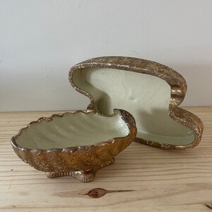 May include: A gold ceramic seashell trinket box with a textured surface. The box is open and the lid is laying next to it.