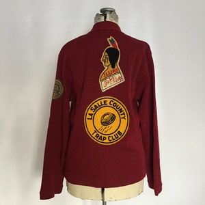 May include: Red long-sleeved shirt with three patches on the back. The patches are yellow, red, and white with the text "ILLINI", "Shady Rest", "LA SALLE COUNTY TRAP CLUB".