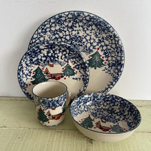 May include: A set of four ceramic dishes featuring a winter scene with a cabin and pine trees. The dishes are decorated with a blue and white speckled glaze.