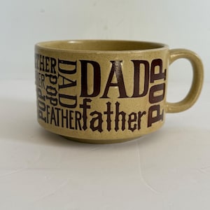 May include: Tan ceramic mug with the word "DAD" in large, dark brown letters. The words "father" and "pop" are also printed on the mug. The mug has a handle and is suitable for hot beverages.