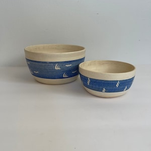 May include: Two ceramic bowls with blue and white patterns. The larger bowl has a white background with a blue band and white birds. The smaller bowl has a white background with a blue band and white swirls.