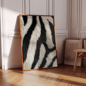 Op de afbeelding: Een ingelijste print van een zwart-wit zebraprintpatroon. De print is in een houten lijst en leunt tegen een witte muur.
