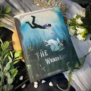 May include: A hardback book titled "The Wicked King" with a fantasy illustration. The cover shows two figures in a watery scene, one reaching for the other. The cover has a teal border and the title is in white script.