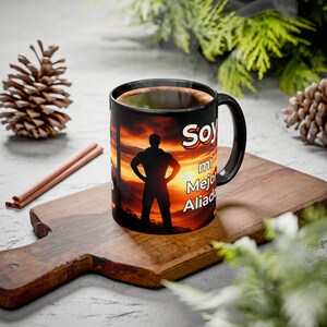 Puede incluir: Taza de café negra con la silueta de una persona frente a una puesta de sol. La taza tiene el texto "Soy mi Mejor Aliado" en blanco. La taza está sobre una tabla de cortar de madera y contiene café caliente.