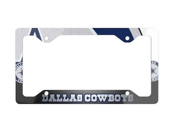 May include: A license plate frame with a white, silver, and navy blue design. The frame features the text "DALLAS COWBOYS" in navy blue and the team's logo. The frame is rectangular with rounded corners.